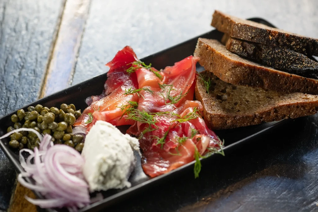 A black plate of salmon, capers, onions, cheese, and rye bread.