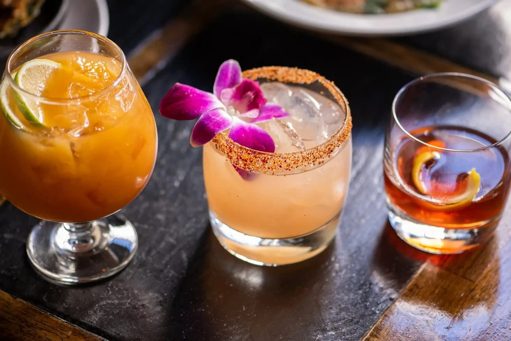 Three cocktails on a dark surface, one with a purple orchid.