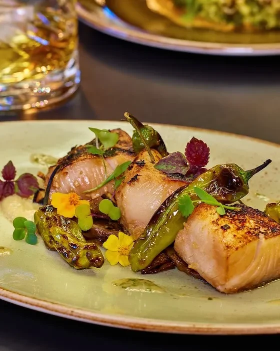 Plated fish with green peppers, edible flowers, and fresh herbs.