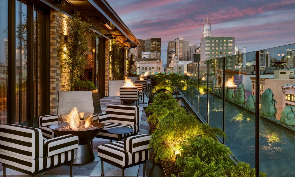 Rooftop patio with striped chairs and fire pits at sunset, city skyline.