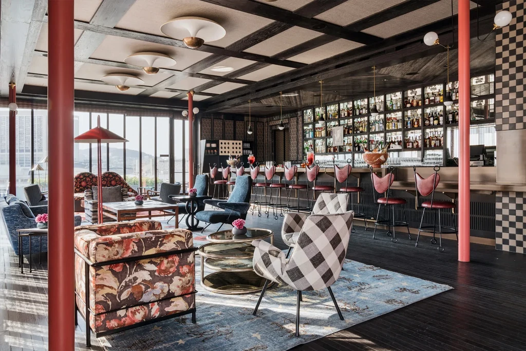 A stylish bar and lounge with patterned chairs, red pillars, and a full bar.