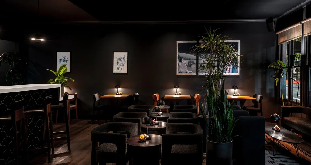 A dark, modern bar or lounge with plants, art, and stylish seating.