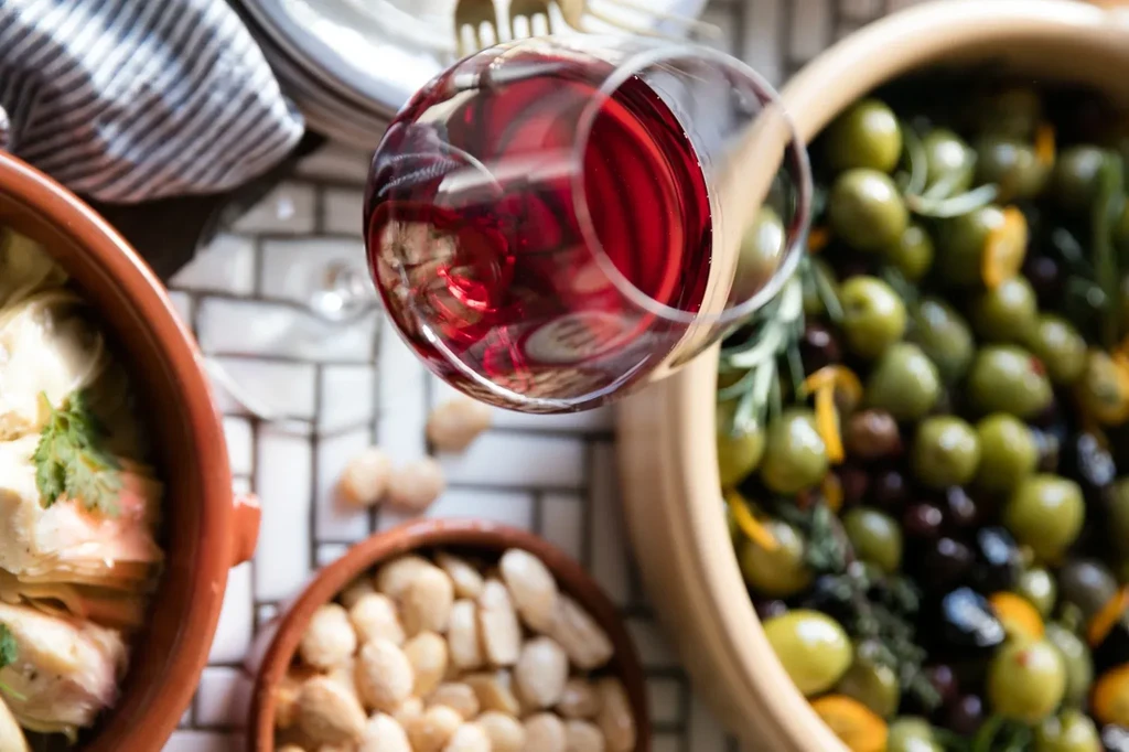 Overhead view of a glass of red wine, olives, almonds, and food.