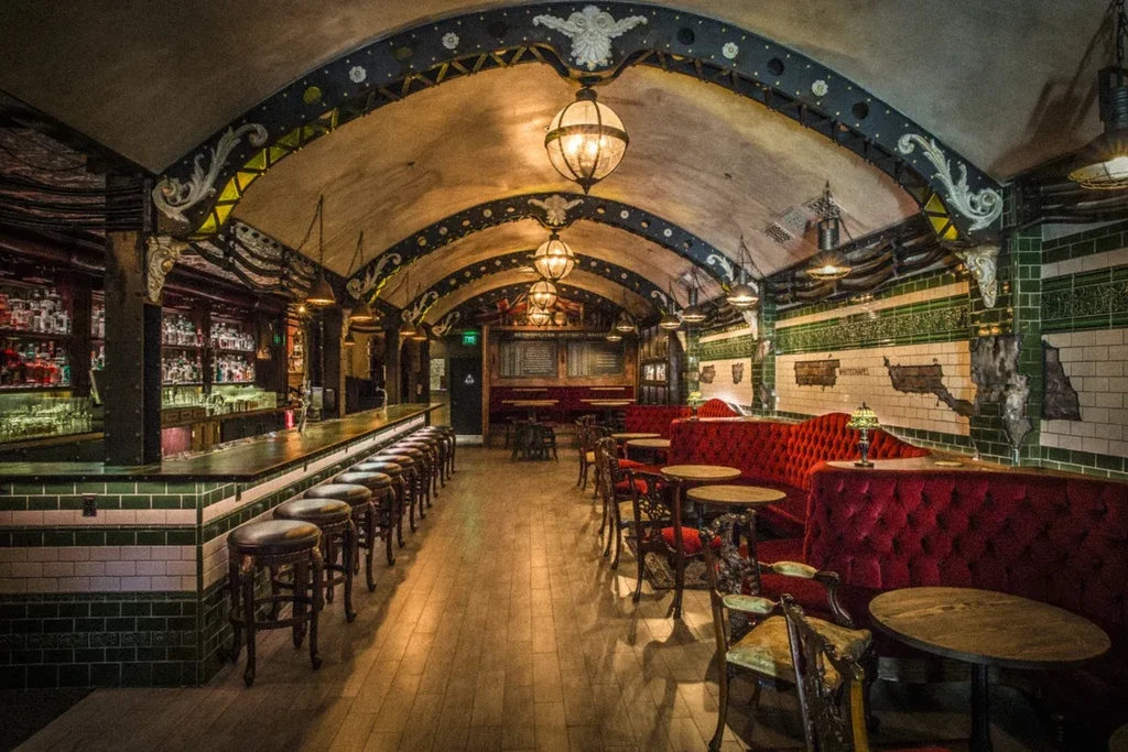 Underground bar with arched ceiling, red velvet booths, and tiled walls.