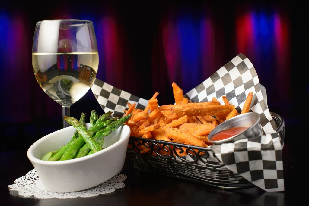 White wine, asparagus, and sweet potato fries with ketchup on a dark table.