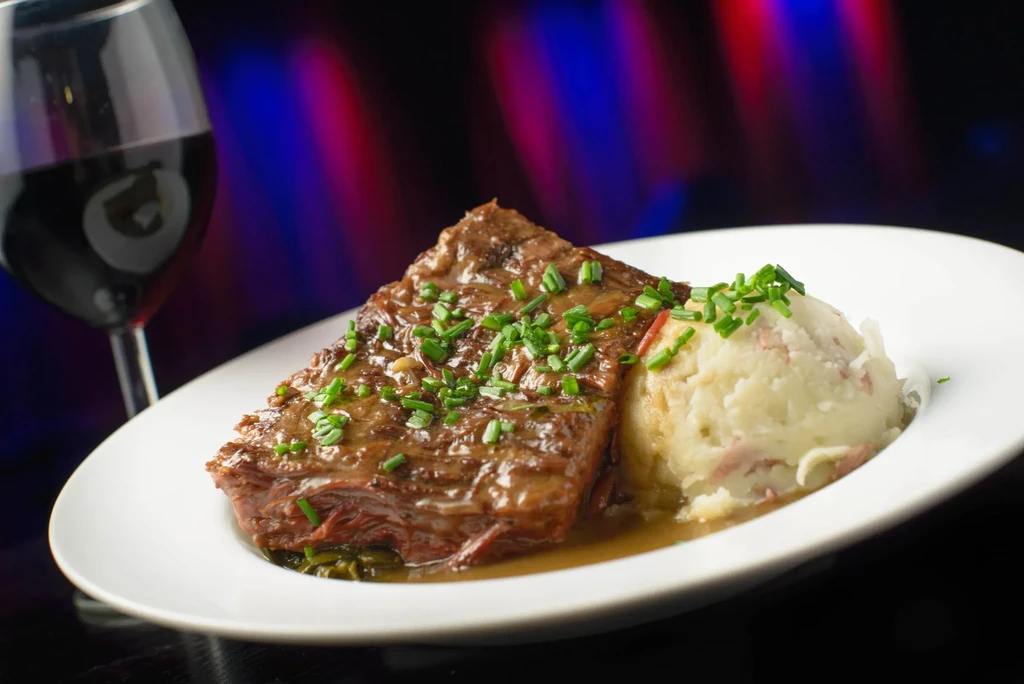 Braised short ribs with mashed potatoes, garnished with chives, and a glass of wine.