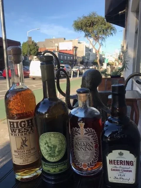 Four liquor bottles on a table with a city street in background.