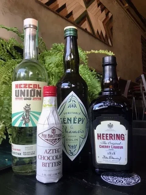 Four bottles of alcohol and bitters on a table with a fern.