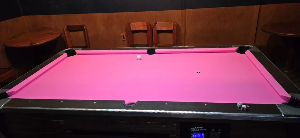 A vibrant pink pool table with a cue ball and a dark brown background.