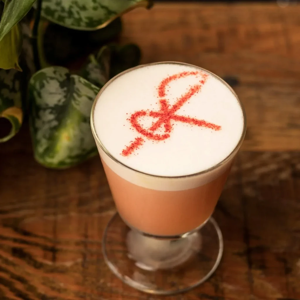 Pink cocktail with foam art on a wooden table.