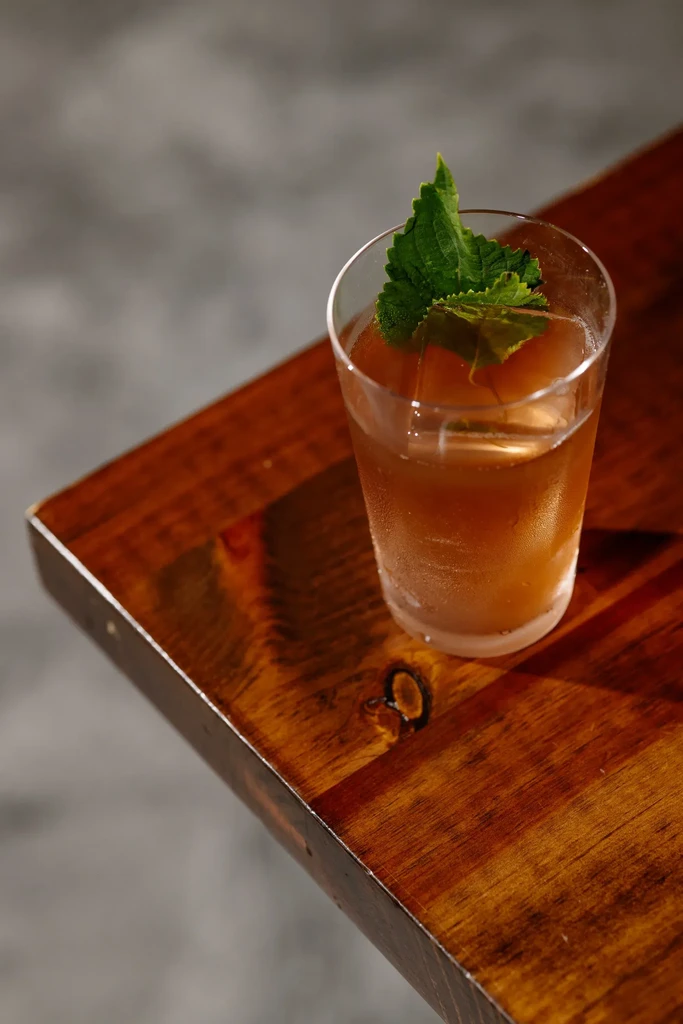 A glass of iced tea with mint leaves on a wooden table.