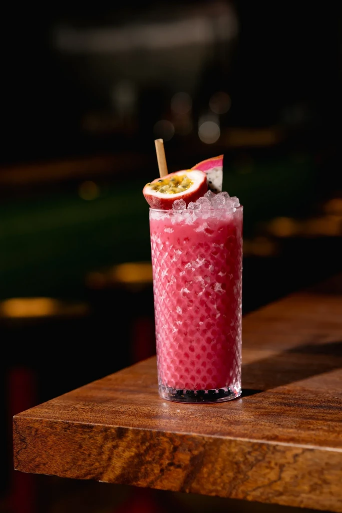 Pink cocktail with passion fruit and dragon fruit garnish.