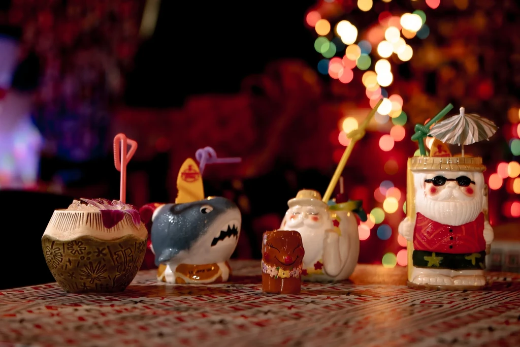 Tiki mugs shaped like Santa, a shark, and a coconut with drinks.