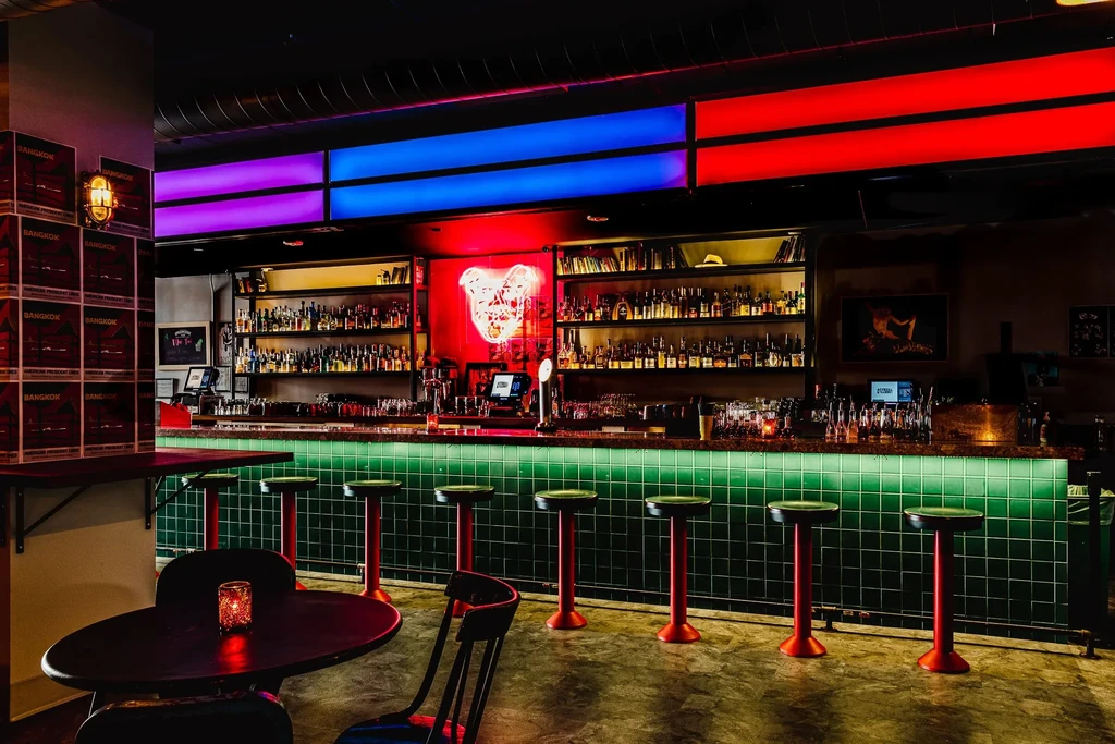 A vibrant bar with red bar stools and colorful overhead lighting.