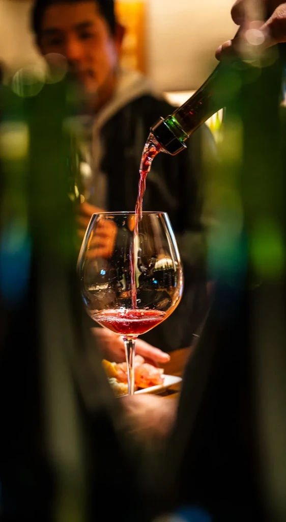 Red wine pours into a glass. A person is out of focus in the background.