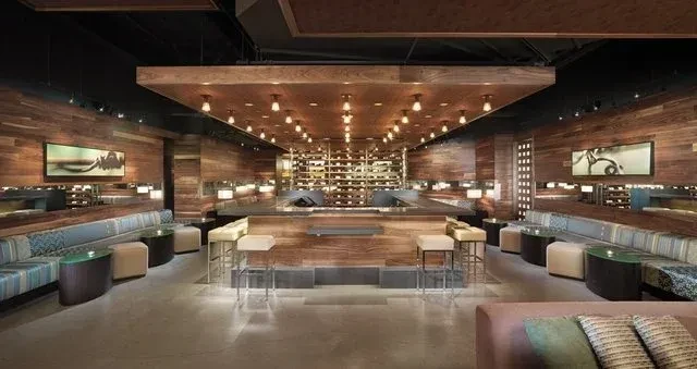 A contemporary bar and lounge with wood walls and backlit wine racks.