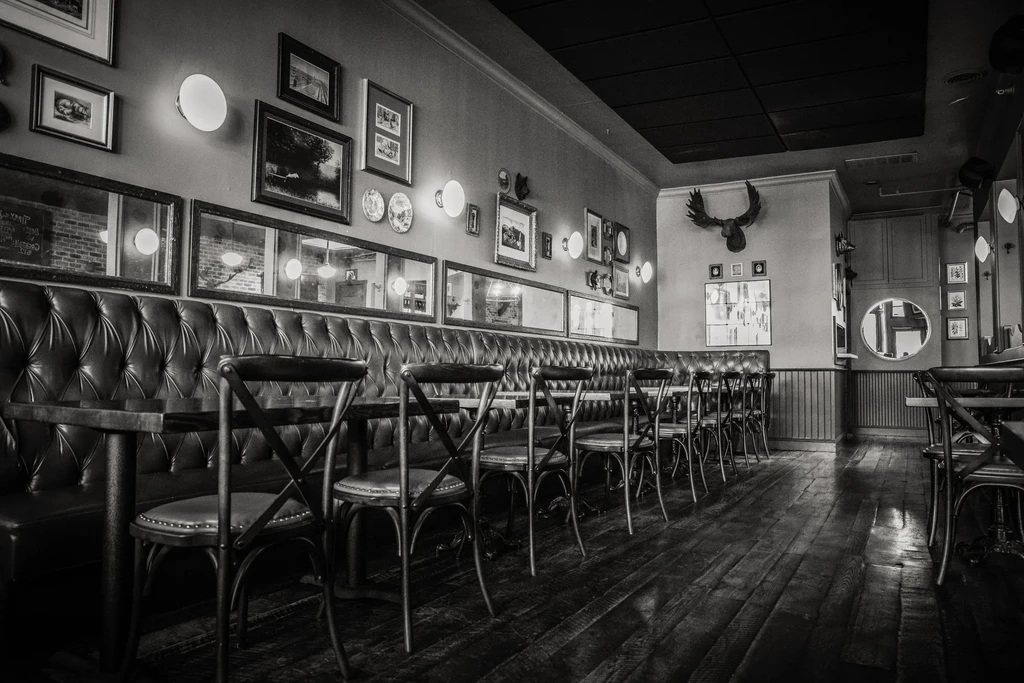 Monochrome image of an empty restaurant with tufted leather seating and chairs.