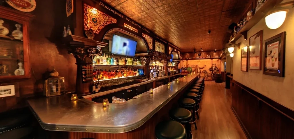 A long, empty bar with dark stools and shelves of liquor.
