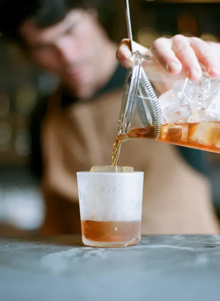 Bartender pours an amber drink from a shaker into a glass with ice.