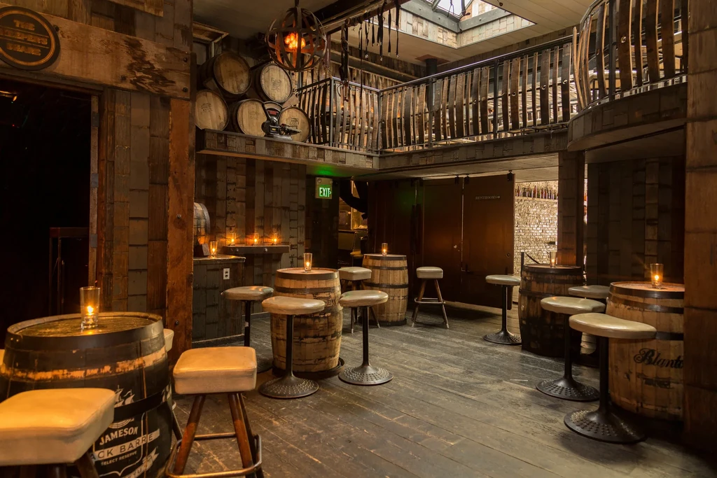 Whiskey barrel tables and bar stools in a rustic, candlelit bar.