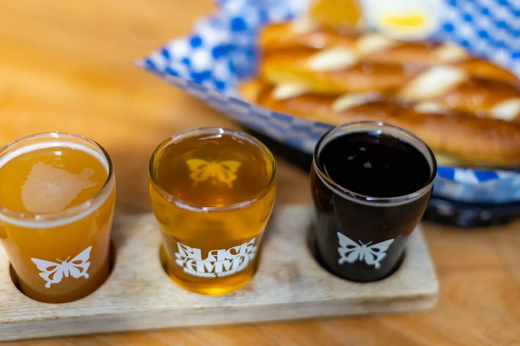 Three glasses of beer on a wooden tray with pretzels in the background.