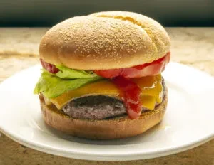 A homemade cheeseburger with lettuce, tomato, and ketchup on a white plate.