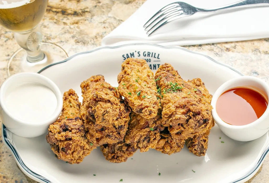 Fried chicken pieces, with dipping sauces, and a beer on a marble table.