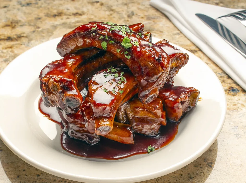 A plate of BBQ ribs covered in sauce and parsley.