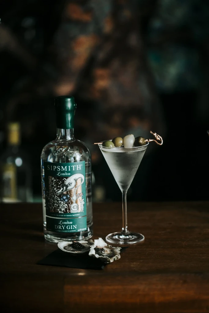 A bottle of gin, a martini, and oysters with caviar on a bar.