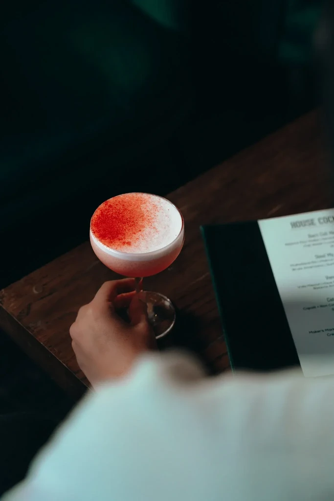 Overhead view of a person holding a red cocktail on a table.