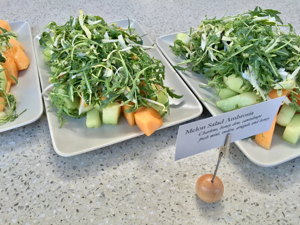 Plates of melon salad with arugula and a descriptive sign.