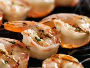 Several grilled peeled shrimp, seasoned with pepper and herbs, cooking on a grill.