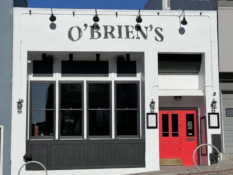 White building with "O'Brien's" sign, dark windows, and red double doors.
