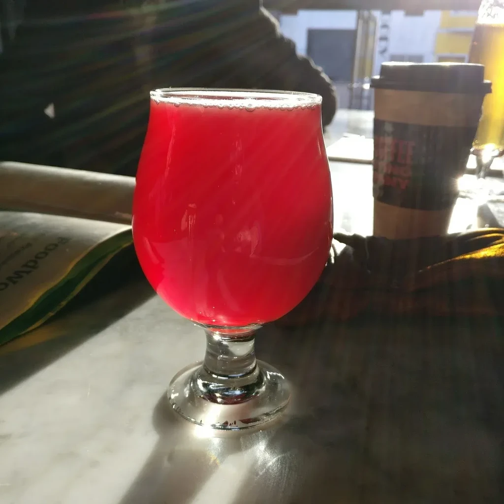 A glass of red beer sits on a marble table in a cafe.