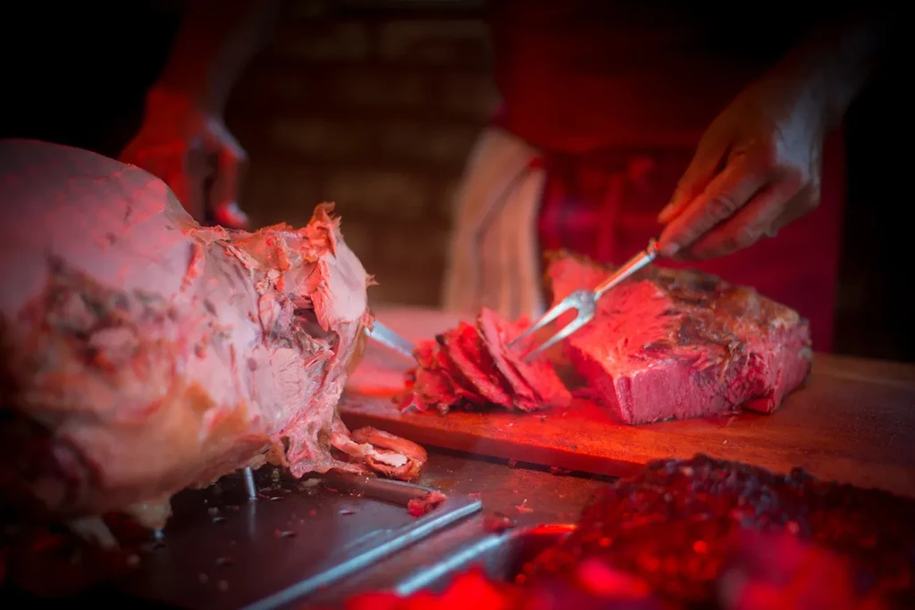 A chef carves slices from a large roast under a red heat lamp.