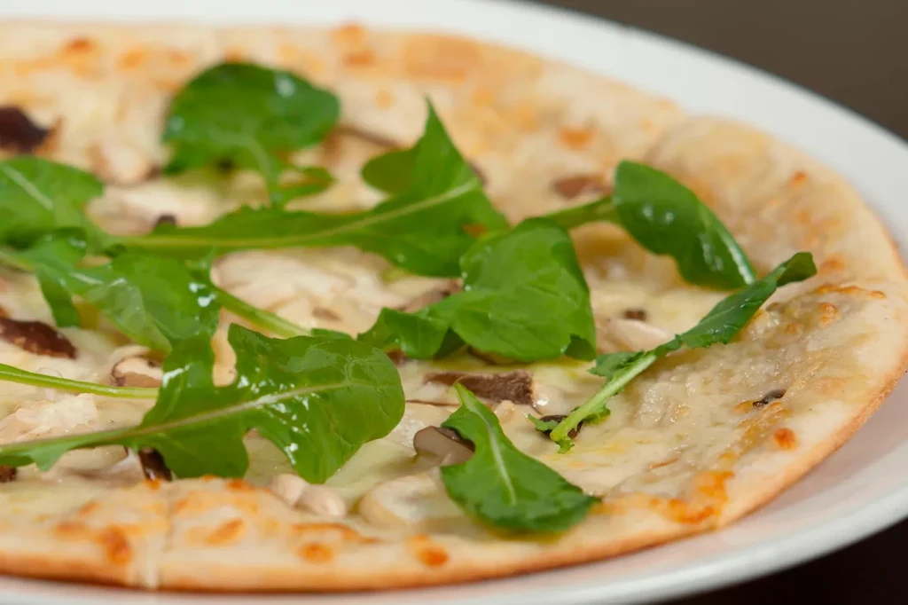 A white pizza with mushrooms, cheese, and fresh arugula on a white plate.