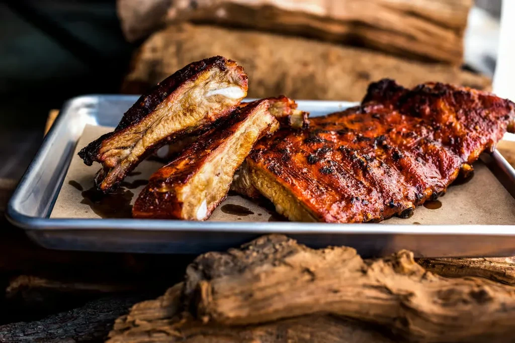 A full rack of glazed ribs and two cut rib pieces on a tray.