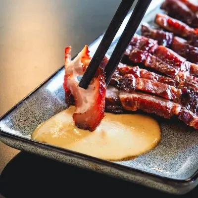 Chopsticks dipping a piece of sliced char siu into sauce.