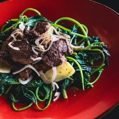 Beef, spinach, and onions served in a red bowl.