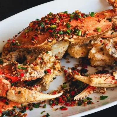 Spicy chili crab served on a white plate with green onions.
