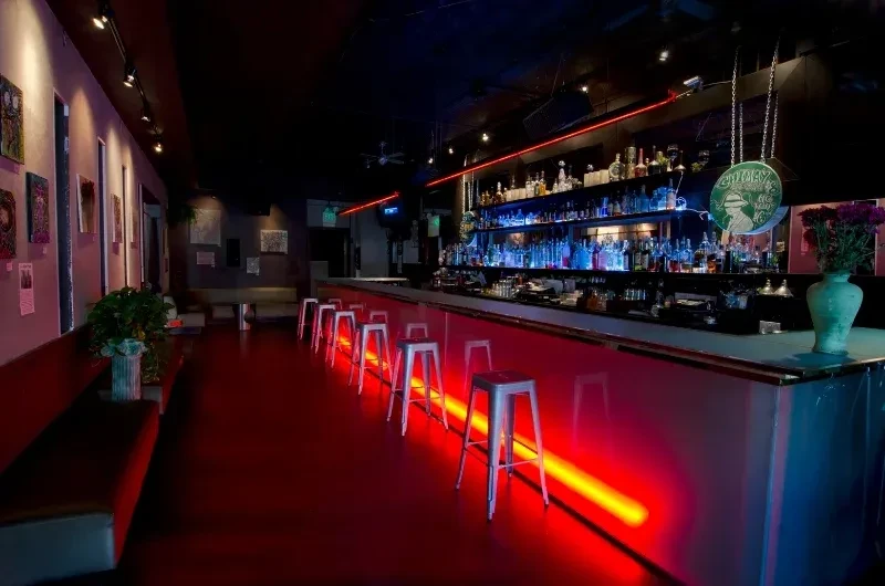 A dim bar with a red floor and neon lighting.
