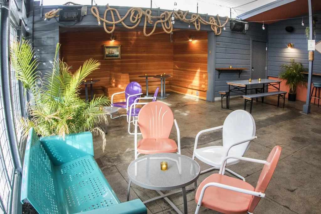 An empty outdoor patio with colorful chairs, tables, and rope decorations.