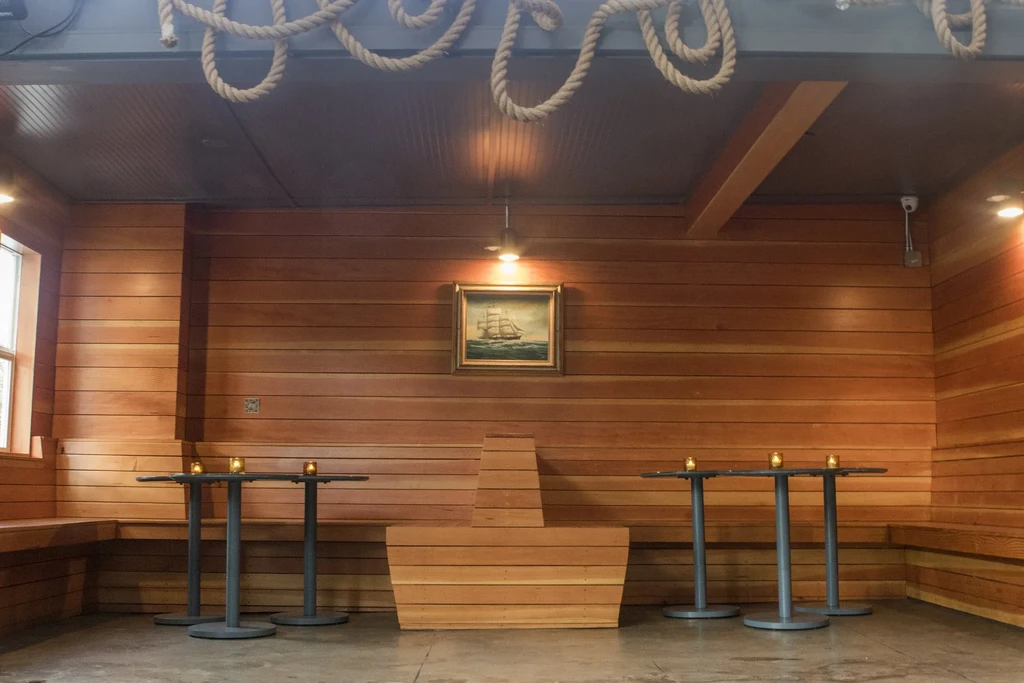 Interior with wood-paneled walls, nautical decor, tall tables, and bench seating.