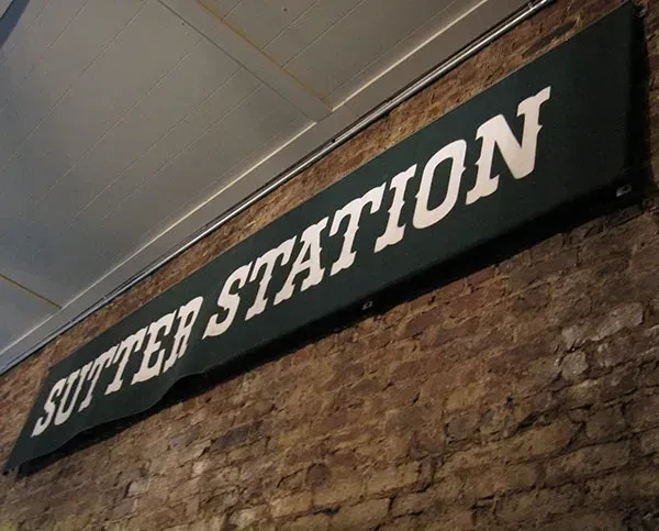 A banner with "Sutter Station" in white letters hangs on a brick wall.