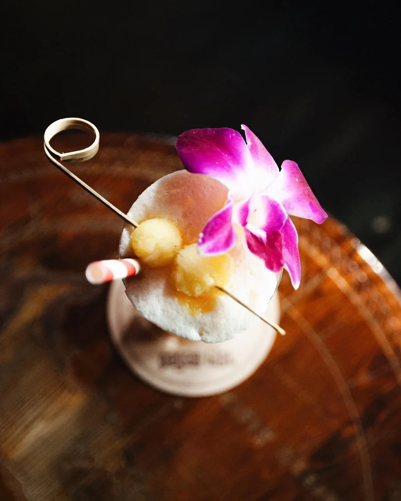Overhead view of a drink garnished with a purple orchid and fruit.