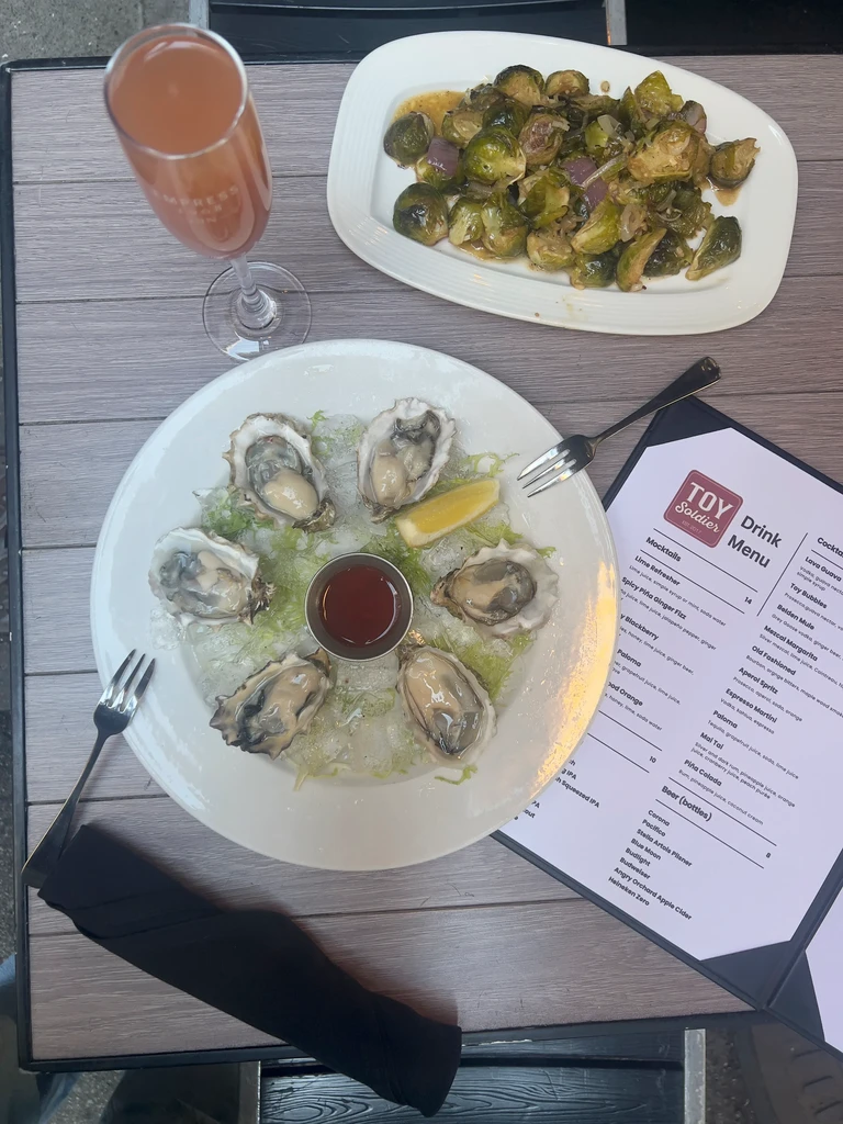A meal of oysters, brussels sprouts, and a drink on an outdoor table.