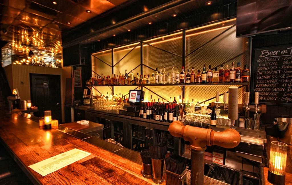A dimly lit bar with a wooden counter and shelves of liquor bottles.