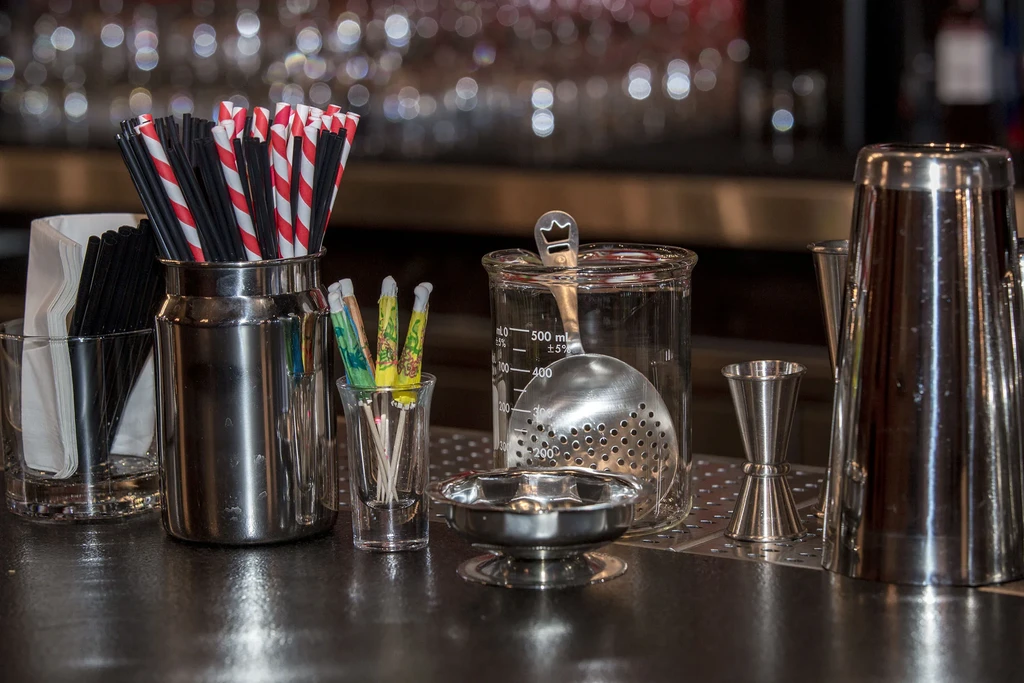 Bar counter with straws, drink umbrellas, and cocktail preparation tools.