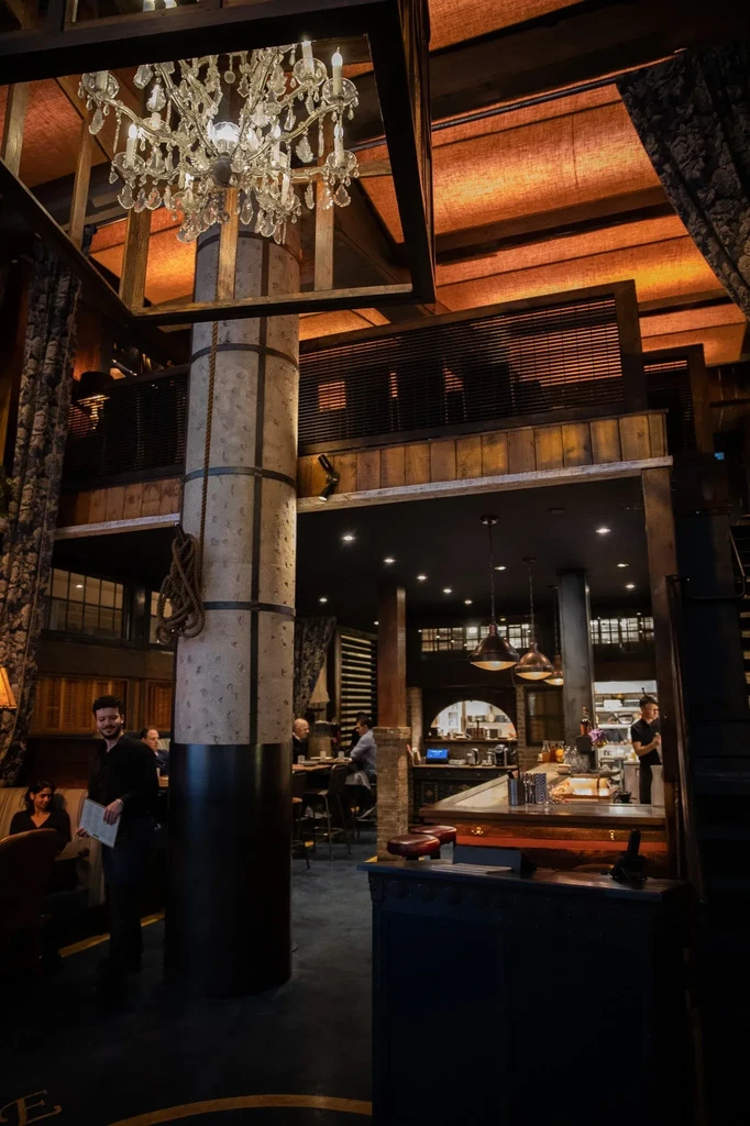 Large restaurant with a crystal chandelier, column, and people dining.