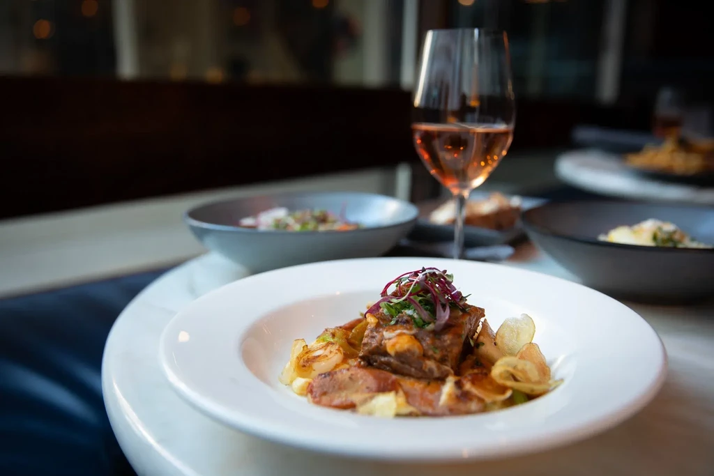 A restaurant table with three bowls of food and a glass of rosé wine.
